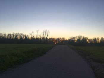 Road amidst field against clear sky during sunset