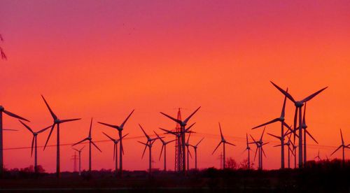 Silhouette wind turbines on field against orange sky