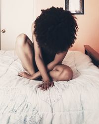 Woman with curly hair sitting on bed at home