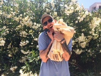 Portrait of man embracing towels standing against plants