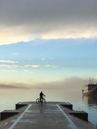 Man riding bicycle on sea against sky