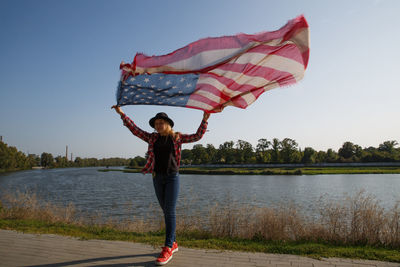 Rear view of woman holding umbrella while standing against lake