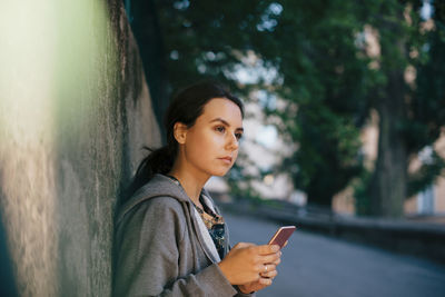 Side view of young woman holding smart phone while looking away