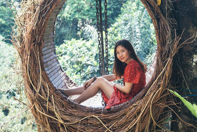 Portrait of smiling woman sitting on swing in forest