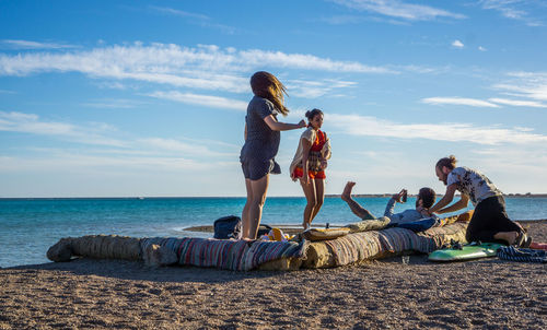 People sitting on beach by sea against sky