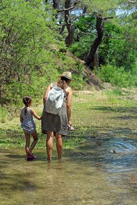 Rear view of mother and daughter wading in river at forest