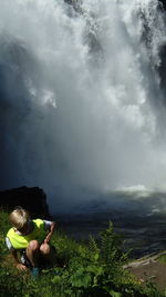 Boy crouching by waterfall