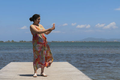 Rear view of woman with arms raised standing at beach against sky