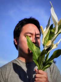 Portrait of young man holding bouquet of white peace lilies against blue sky.