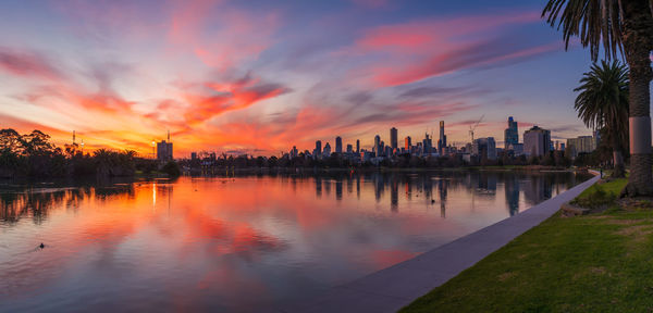 Scenic view of lake by buildings against sky during sunset