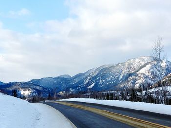 Road leading towards snowcapped mountains against sky