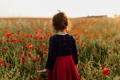 Rear view of woman standing amidst flowering plants on field against sky