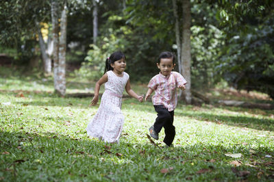 Siblings running on grassy field at park