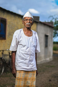 Portrait of senior man in traditional clothing standing against house