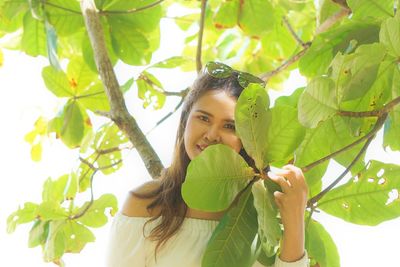 Portrait of young woman holding leaves standing outdoors