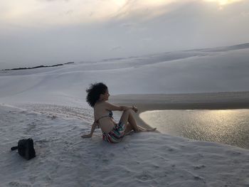 Woman sitting on beach against sky