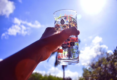 Cropped image of hand holding drink against sky