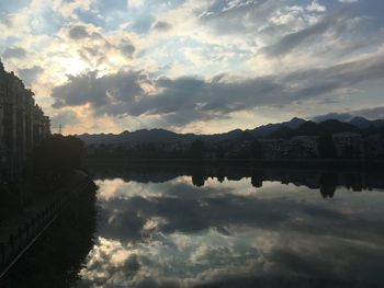 Scenic view of lake by buildings against sky during sunset