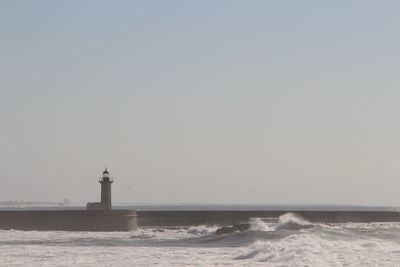 Lighthouse on pier in sea against clear sky