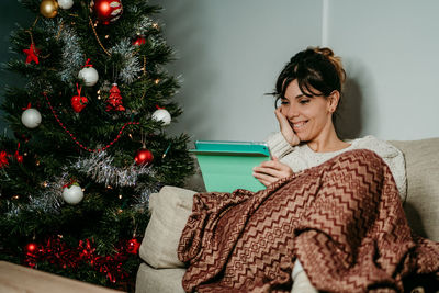 Portrait of young woman with christmas tree at home