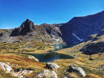 Scenic view of lake and mountains against clear blue sky