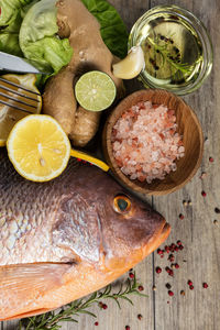 Fresh raw red snapper fish with spices, herbs and vegetables for cooking on wooden background. 