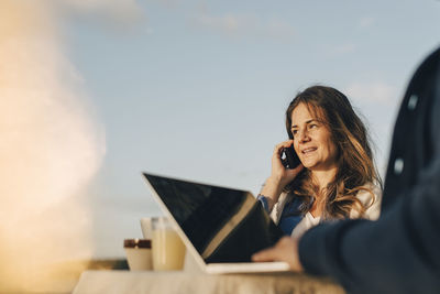 Thoughtful woman using mobile phone while sitting with man against sky