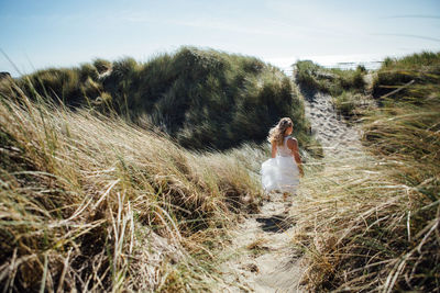 Rear view of young woman walking on trail leading towards beach