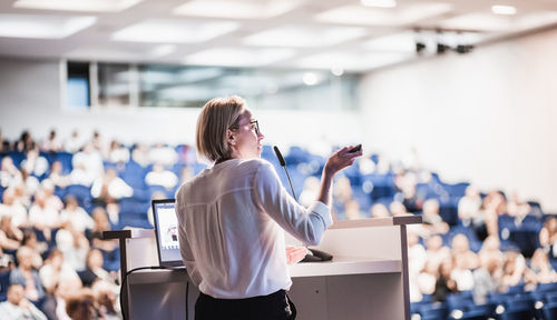 Female speaker giving a talk on corporate business conference. unrecognizable people in audience at