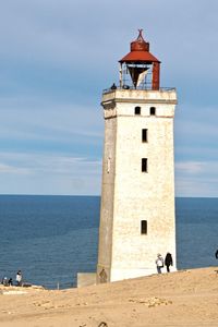 Lighthouse on beach by sea against sky