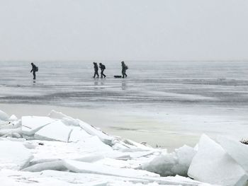 People walking on frozen sea against sky
