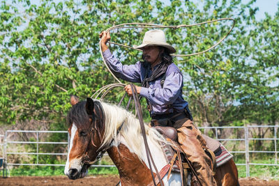 Cowboy holding rope while riding horse at ranch