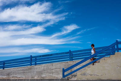 Low angle view of man walking up stairs against blue sky