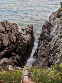 Low section of man sitting on cliff against sea