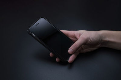Close-up of hand holding mobile phone over black background