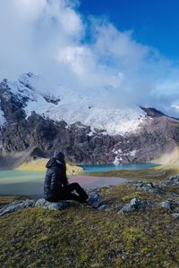 Side view of man sitting on rock against sky