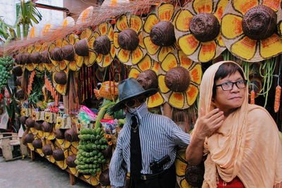 Mature woman wearing headscarf and statue by hats at market for sale