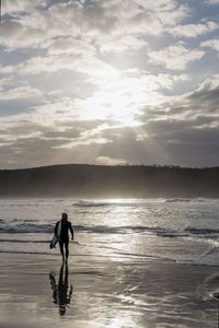 Silhouette people walking at beach against sky during sunset