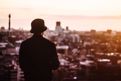Rear view of man wearing hat looking at cityscape during sunset