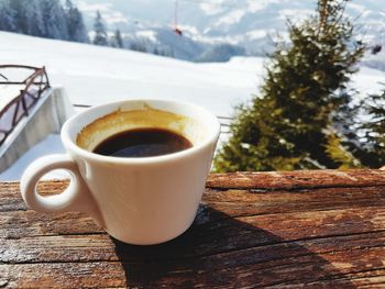 Close-up of coffee cup on table with winter scenery and mountains in the background 