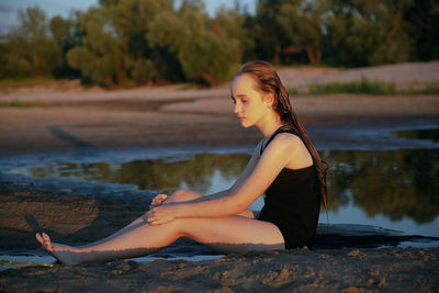 Side view of teenage girl sitting by lake