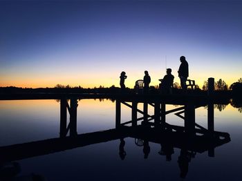 Silhouette people standing by lake against clear sky at sunset