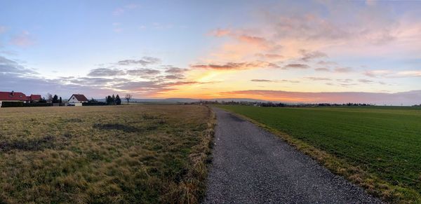 Road amidst field against sky during sunset