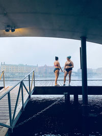 Rear view of men standing on railing against sea