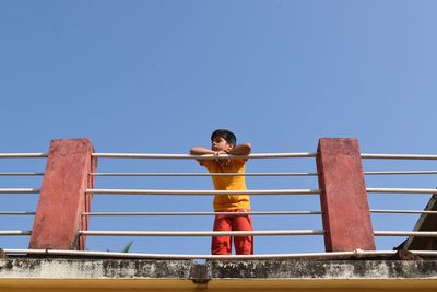 Low angle view of shirtless man against railing against clear blue sky