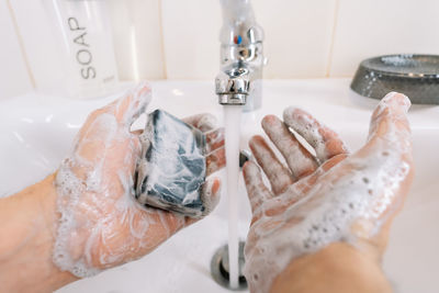 Close-up of hands washing with black soap in sink in bathroom