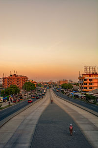 Road by city against sky during sunset