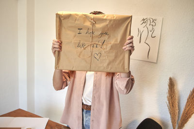 Midsection of man holding paper while standing against wall at home