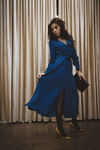 Full length of young woman standing against curtain