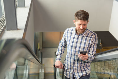 Male traveler using smartphone on escalator